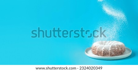 Icing sugar falling of fresh home made bundt cake. Powder sugar falls on fresh bunt cake over blue background. Copy space for text. Ideas and recipes for breakfast or dessert. Banner Royalty-Free Stock Photo #2324020349
