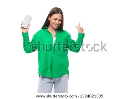 pretty slender european brunette woman with long hair and brown eyes dressed in a casual green shirt points her finger up holding a smartphone in her phone