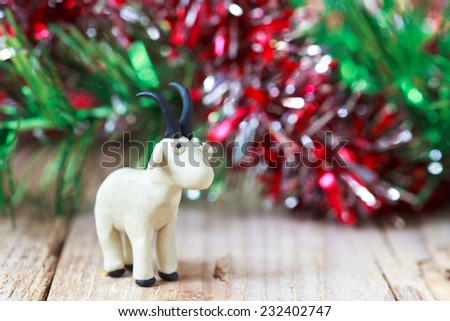 Plasticine world - little homemade white goat with black horns and hooves stand on a wooden floor, selective focus and place for text