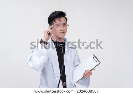 Portrait of a young and professional doctor, medical student, intern, thinking while holding a pen and a clipboard. Isolated on a white background. Royalty-Free Stock Photo #2324038587