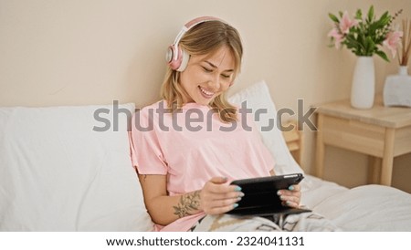 Young blonde woman watching video sitting on bed at bedroom