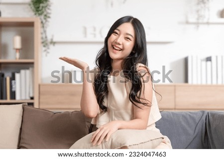 Happy attractive asian young woman smile and open hand palm to copy space at home. Cheerful pretty girl wear casual dress open palm to empty space for mockup to display product