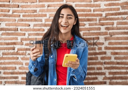 Young teenager girl wearing student backpack using smartphone smiling and laughing hard out loud because funny crazy joke. 