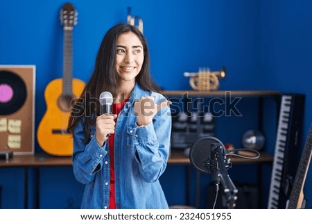 Young teenager girl singing song using microphone pointing thumb up to the side smiling happy with open mouth  Royalty-Free Stock Photo #2324051955