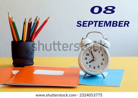 Calendar for September 8: numbers 08, the name of the month September in English, a white alarm clock, school supplies on the table on a light background