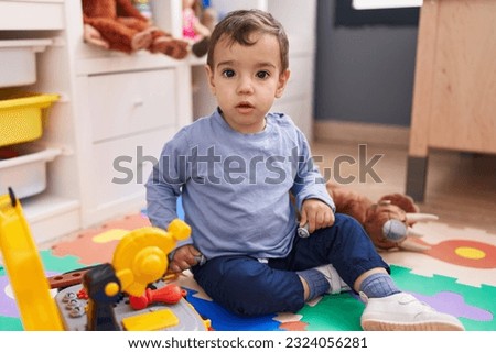 Adorable hispanic boy playing with tools toy sitting on floor at kindergarten