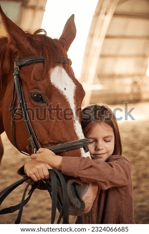 Embracing the animal. Cute little girl is with horse indoors.