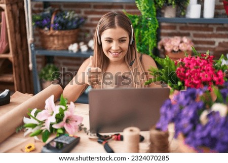 Young blonde woman working at florist shop doing video call smiling happy and positive, thumb up doing excellent and approval sign 