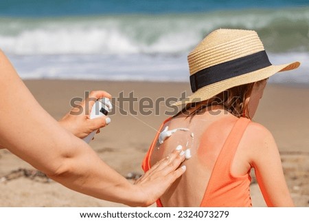 Mother spraying panthenol foam on her daughter's sunburnt back on a beach Royalty-Free Stock Photo #2324073279