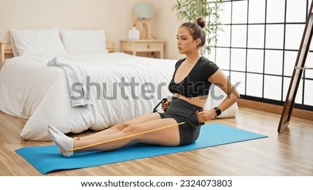 Young beautiful hispanic woman training with elastic band at bedroom