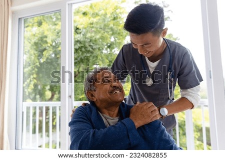 Happy diverse male doctor discussing with senior male patient in wheelchair at home. Medical services, check up, home visit, healthcare, wellbeing and senior lifestyle, unaltered.