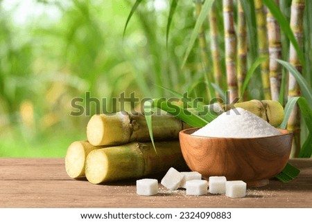 White sugar with fresh sugar cane on wooden table with sugar cane plantation farming background. Royalty-Free Stock Photo #2324090883