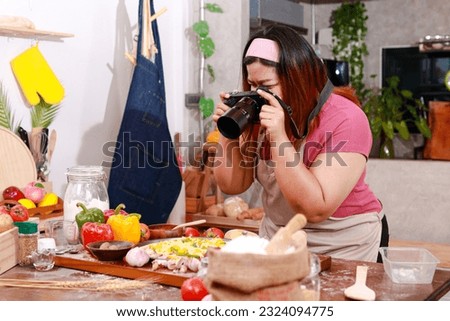 Fat girl cooking in the kitchen holding a camera to take pictures of food placed on the table. Food concept. Chef cooking
