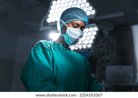 African american female surgeon wearing surgical gown and face mask in operating theatre. Hospital, surgery, medicine, healthcare and work, unaltered. Royalty-Free Stock Photo #2324103367