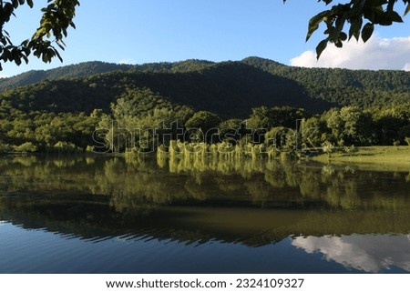 Impressive lake picture with mountains and trees in the background. Cloudy weather. Calm water.