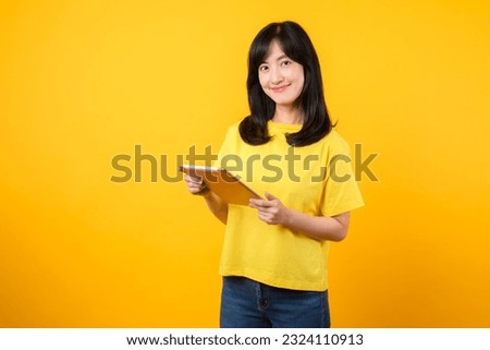 Experience the joy of education technology with portrait. A Asian young woman wearing a yellow t-shirt and denim jeans showcases a happy smile while using digital tablet. education technology concept.