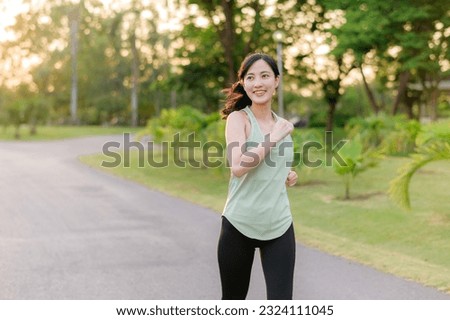 Fit young Asian woman jogging in park smiling happy running and enjoying a healthy outdoor lifestyle. Female jogger. Fitness runner girl in public park. healthy lifestyle and wellness being concept Royalty-Free Stock Photo #2324111045