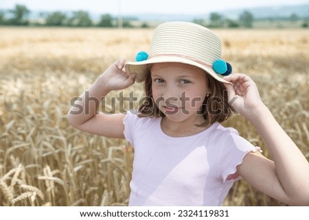little blonde girl in a hat and a pink dress, standing on a wheat field and touching the ears of wheat with her hands. child enjoying nature wheat field.Happy moments