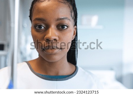 Portrait of african american female patient with braids, wearing hospital gown, holding drip. Hospital, medicine, healthcare and work, unaltered.