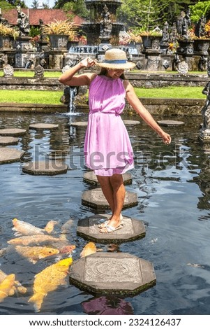 Woman traveler wearing white dress and straw hat at  Taman Tirtagangga temple on Bali, Indonesia in a sunny day Royalty-Free Stock Photo #2324126437