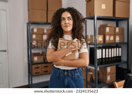 Young hispanic woman working at small business ecommerce smiling looking to the side and staring away thinking. 