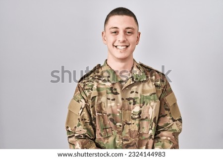 Young man wearing camouflage army uniform with a happy and cool smile on face. lucky person. 