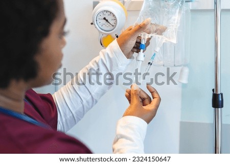 African american female doctor wearing scrubs, applying drip in hospital room. Hospital, medicine, healthcare and work, unaltered.