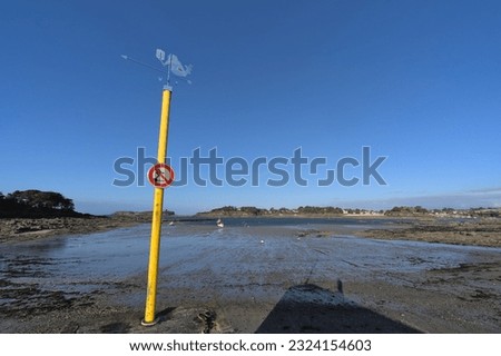 January 13, 2023, Lancieux, Brittany, France: "No swimming" sign and mermaid-shaped spinner at en of pier at sand beach during low tide 