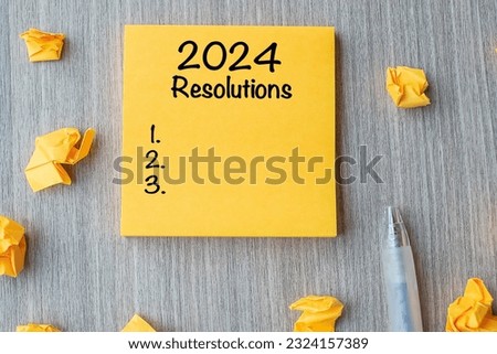 2024 RESOLUTIONS word on yellow note with pen and crumbled paper on wooden table background. New start, Strategy and Goal concept