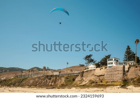 Pismo Beach cliffs and silhouette of a skydiver with parachute open, and bright blue sky in the background, California Coastline