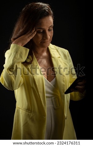Coaching woman, wearing yellow outfit, looking at news on cell phone. Communicative and motivational management. Isolated on black background.