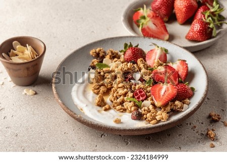Healthy breakfast: fresh granola, muesli with yogurt, strawberry and honey on beige textured background. Copy space. Horisontal