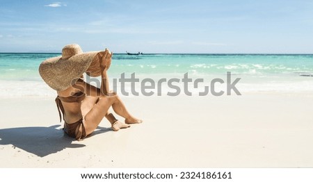 Back view of woman on tropical vacation relaxing  on the sandy beach with turquoise water, wearing bikini and summer hat. Paradise in Thailand. Asia. Traveler. Wanderlust.
