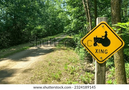 Funny sign denoting a tractor crossing.  Concepts could include agriculture, country life, humor, other.