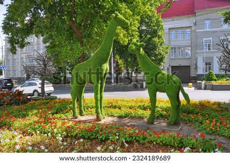 Art object two artificial grass giraffes stand among trees and flowers in a city park