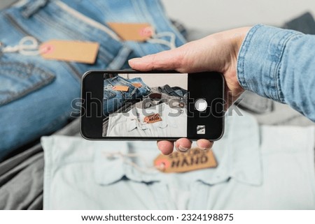 View of womans hand taking photo of denim clothes to upload in second hand fashion app on the smartphone. Sell, buy and swap clothes online