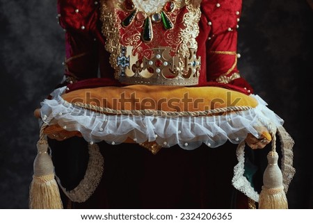 Closeup on medieval queen in red dress with crown on pillow on dark gray background. Royalty-Free Stock Photo #2324206365
