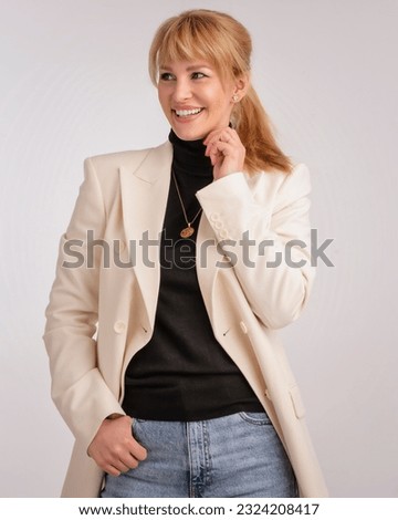 Portrait of an attractive woman smiling and looking at camera. Blond haired female wearing blazer and standing against isolated background. Copy space. Studio shot. 
