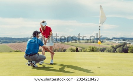 Pro on golf course teaching a woman how to put Royalty-Free Stock Photo #2324218423