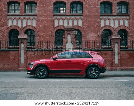 Red car, crossover type, parked in the street, side view on brick building symmetrical background Royalty-Free Stock Photo #2324219119