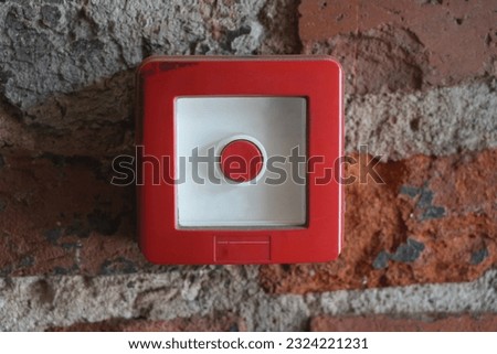 Single red emergency button on the old worn out red brick wall, red button, caution sign, red alert, alarm safety button with panic and emergency control warning on the wall