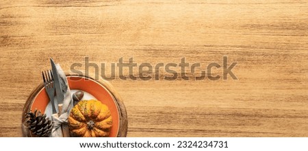 A plate with cutlery is decorated for Thanksgiving with pumpkins and autumn products on a wooden table, top view