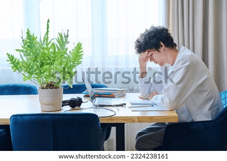 Tired sad guy student sitting at desk at home with laptop