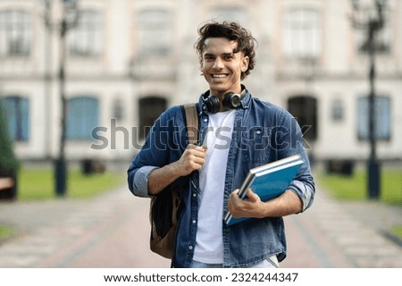 Portrait of happy handsome student guy with backpack and workbooks posing outdoors over university building background, cheerful young male looking at camera and smiling, free space Royalty-Free Stock Photo #2324244347
