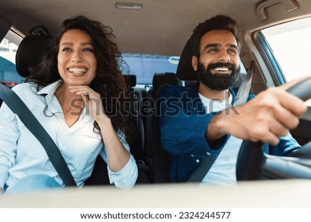 Happy arab couple going on summer vacation by car, man and woman sitting in their new auto, cheerfully smiling looking at road, making test drive in the city Royalty-Free Stock Photo #2324244577