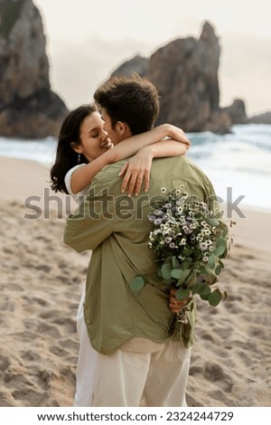 Young couple in love embracing having romantic date on beach, man holding flowers behind his back, giving gift to his girlfriend, vertical shot Royalty-Free Stock Photo #2324244729