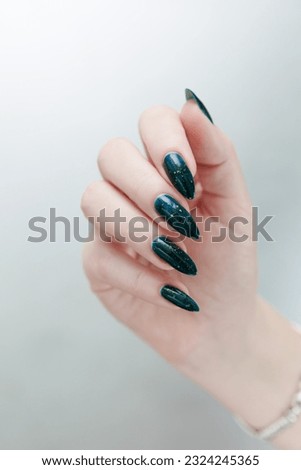 Woman's beautiful hand with long nails and dark teal, blue and green nail polish