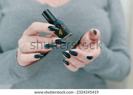Woman's beautiful hand with long nails and dark teal, blue and green nail polish
