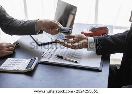 Car rental service concept. Close up view Hand of agent giving car key to customer after signed rental contract form.Close-up partial view of dealer giving car key to new owner