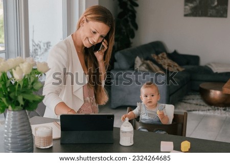 Working happy woman using tablet and having phone call near little daughter